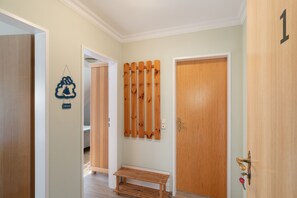 Een gang met een houten bankje, een deur met een nummer en een bord met een welkomstboodschap.