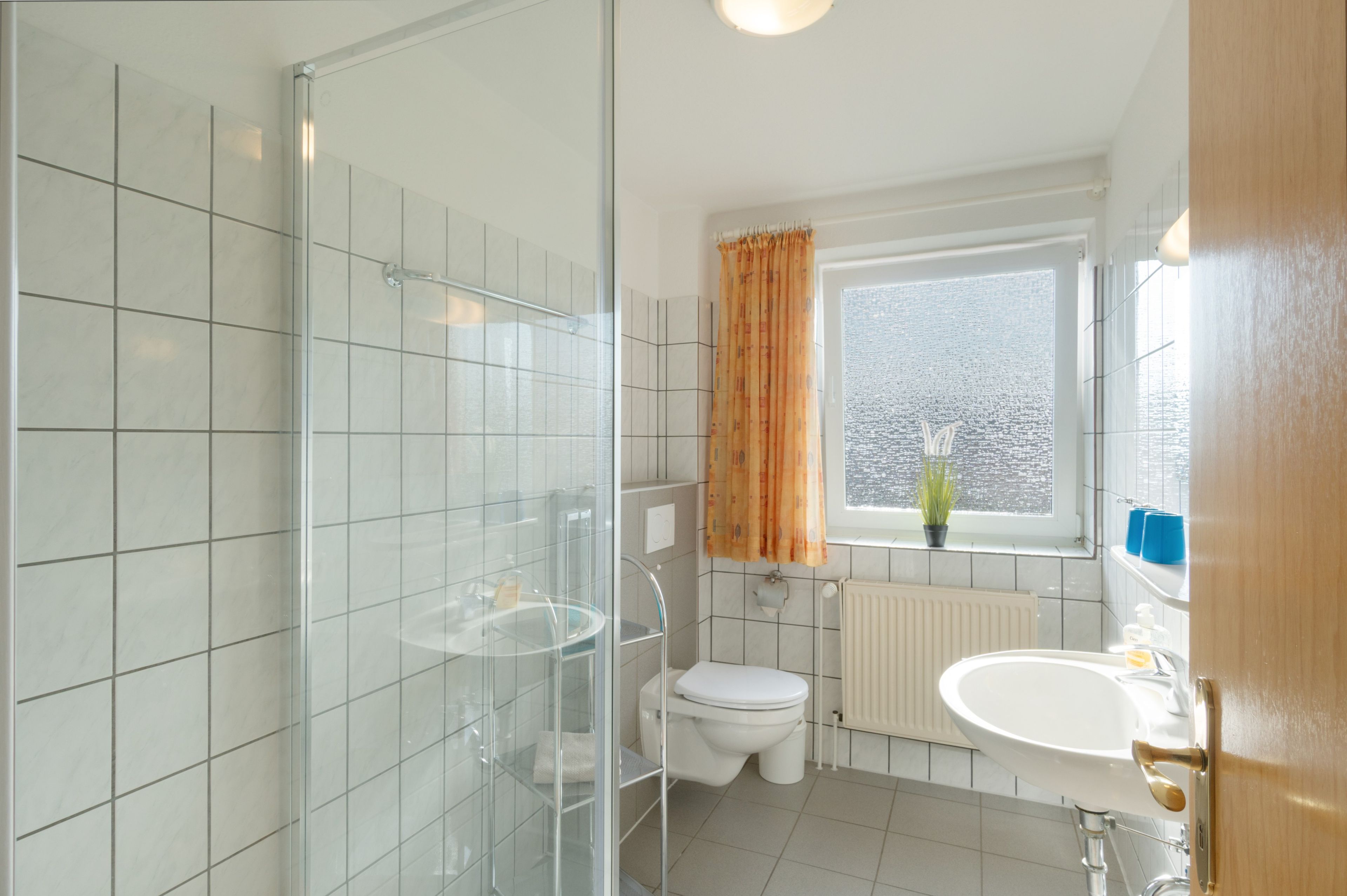 Ein modernes Badezimmer mit Duschkabine aus Glas, Toilette, Waschbecken und einem Fenster mit Vorhängen.