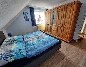 A bedroom with a bed, a wooden wardrobe, and a window with curtains. - Apartment 'Haus Hanning 1' with Shared Garden and Wi-Fi (Wangerland)