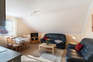 Een moderne woonkamer met een zwarte leren bank, een houten salontafel, en een eethoek met een tafel en stoelen.