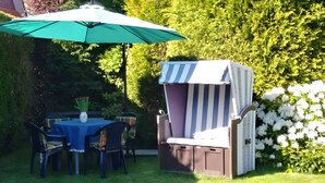 Eine Terrasse im Freien mit Tisch, Stühlen, einem gestreiften Grill und einem grünen Sonnenschirm.
