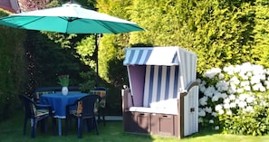 An outdoor patio with a table and chairs, a striped grill, and a green umbrella. - Apartment 'Haus Hanning 1' with Shared Garden and Wi-Fi (Wangerland)
