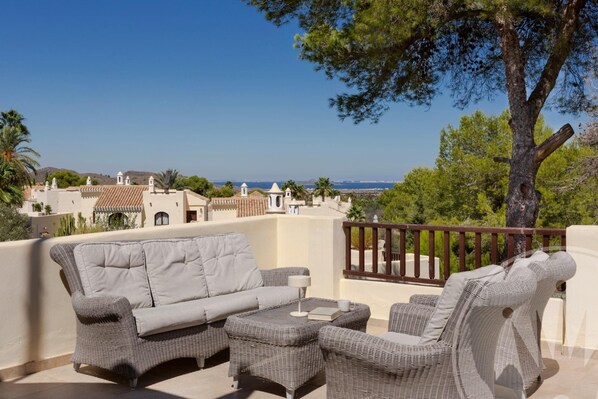 Ein Balkon mit Korbmöbeln, Blick aufs Meer und Gebäude im Hintergrund.