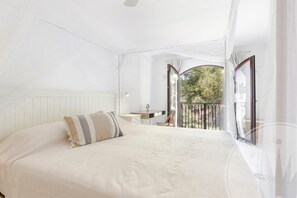 Ein Schlafzimmer mit einem großen Bett, einem Nachttisch, einem Sessel und Blick ins Freie durch ein Fenster.