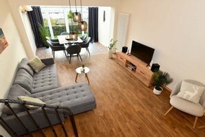 Ein modernes Wohnzimmer mit einer Couch, einem Esstisch mit Stühlen, einem Fernseher und einer Treppe.