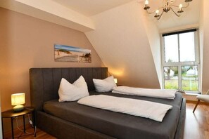 Een slaapkamer met een bed, nachtkastje, lamp, schilderij aan de muur en een raam.