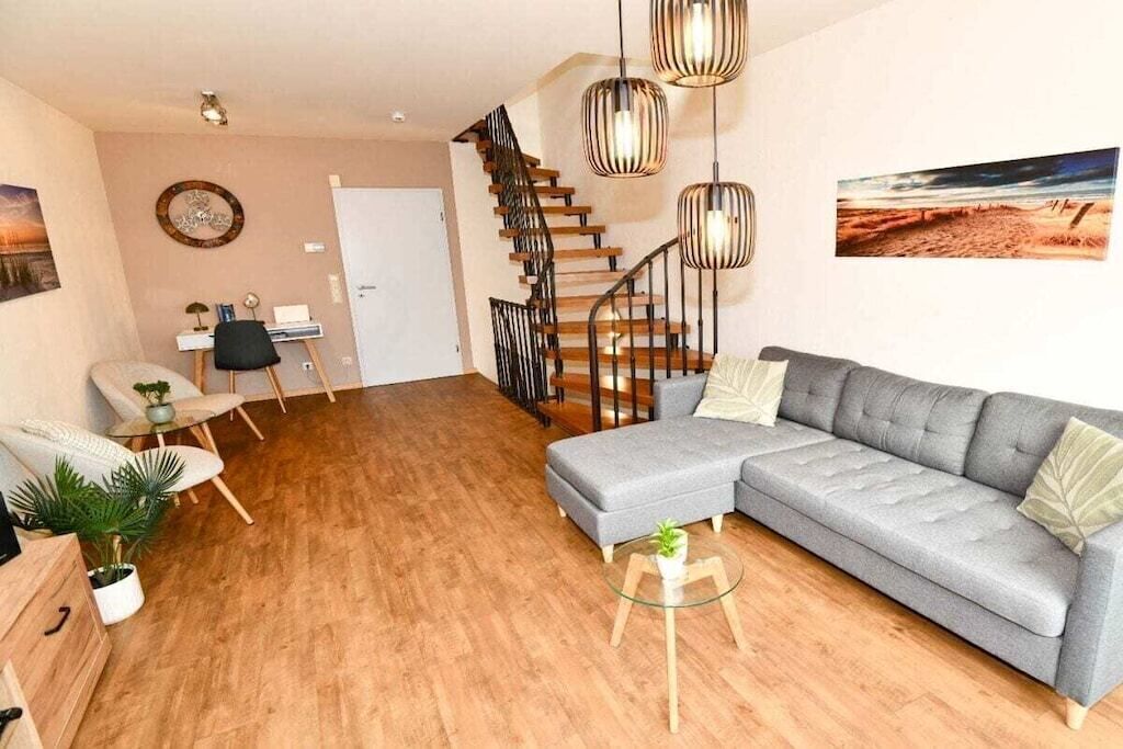 Un salon moderne avec un canapé d’angle gris, un escalier en bois et une table basse en verre.