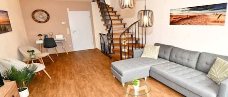 A modern living room with a grey sectional sofa, a wooden staircase, and a glass coffee table.