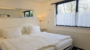 Un letto matrimoniale con testiera, un comodino, uno specchio fissato al muro, una finestra con tenda e un termosifone.