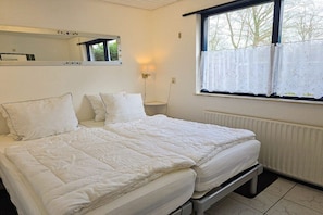 A double bed with a headboard, a bedside table, a wall-mounted mirror, a window with a curtain, and a radiator. - Holiday home with 2 bedrooms (Oostkapelle)