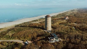 Paesaggio costiero con una torre d'acqua, una spiaggia e un edificio circondato da alberi.