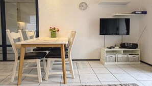 Un'area pranzo con tavolo e sedie, un orologio a parete, un televisore e cesti portaoggetti.