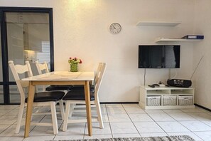 A dining area with a table and chairs, a clock on the wall, a television, and storage baskets. - Holiday home with 2 bedrooms (Oostkapelle)