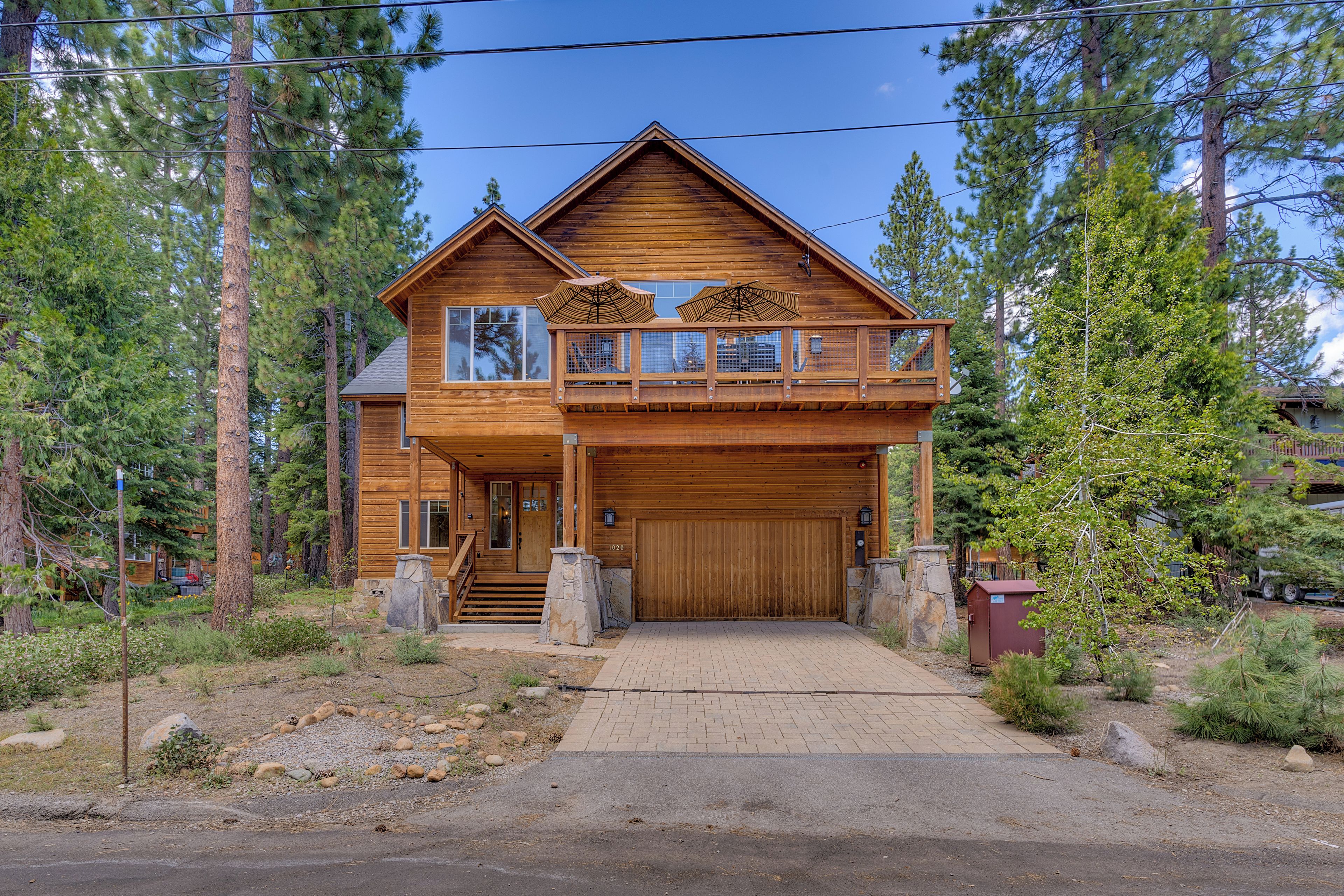 A two-story log cabin with a balcony, a garage, and a stone foundation.