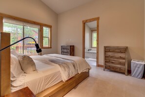 Ein Schlafzimmer mit einem großen Bett, einer Holzkommode, einem Spiegel und Blick auf eine Terrasse und Bäume.