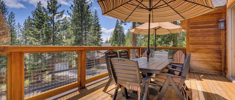 A wooden deck with a table and chairs, a striped umbrella, and a view of trees.