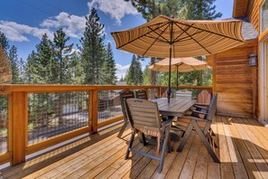 A wooden deck with a table and chairs, a striped umbrella, and a view of trees. - Spacious 5BR Kings Beach Lodge with Mountain Views and Two Living Rooms (Kings Beach)