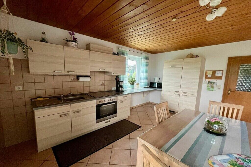 Une cuisine moderne avec des meubles en bois, un four encastré et un coin repas comprenant une table et des chaises.