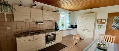 A modern kitchen with wooden cabinets, a built-in oven, and a dining area with a table and chairs.