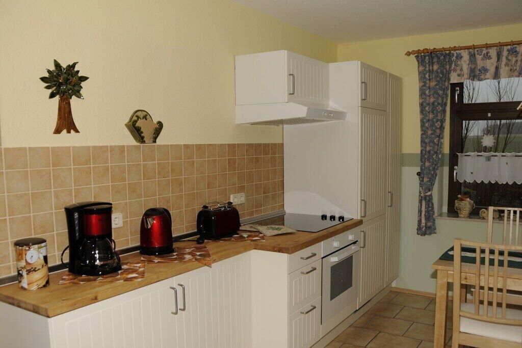 Eine Küche mit weißen Schränken, einer Holz Arbeitsplatte, einer Kaffeemaschine, einem Toaster und einem Fenster mit Vorhängen.