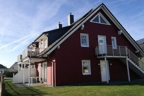 Ein zweistöckiges Haus mit Balkon, einer Haustür und einer Treppe, die zu der oberen Etage führt.