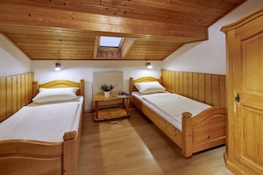 Ein Zimmer mit zwei Holzbett, einem kleinen Tisch mit einer Pflanze und einem Oberlicht.
