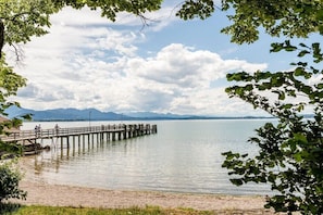 Eine Holzstege führt in einen ruhigen See, im Hintergrund sind Berge zu sehen.