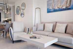 Ein modernes Wohnzimmer mit einer Couch, Sesseln, einem Couchtisch und einem Bild von Segelbooten an der Wand.