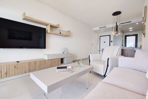 Un salon moderne avec un téléviseur à écran plat, un canapé blanc, une table basse et un mur décoratif en bois.