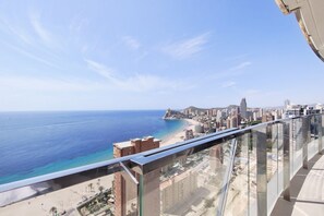 Un immeuble de grande hauteur doté d’un balcon en verre offrant une vue sur une plage et le paysage urbain.