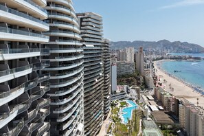 Ein Hochhaus mit mehreren Balkonen, einem Strand und einem Poolbereich.