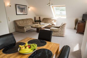 A cozy living room with a sofa set, a coffee table, and a dining table with fruit. - Forest holiday apartment Hamburg 1 (Rosengarten)