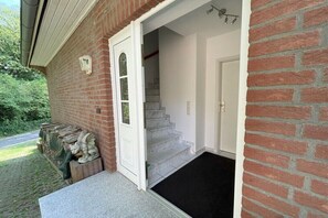 Une façade en briques avec une porte blanche, un paillasson noir et un escalier menant à l’intérieur.