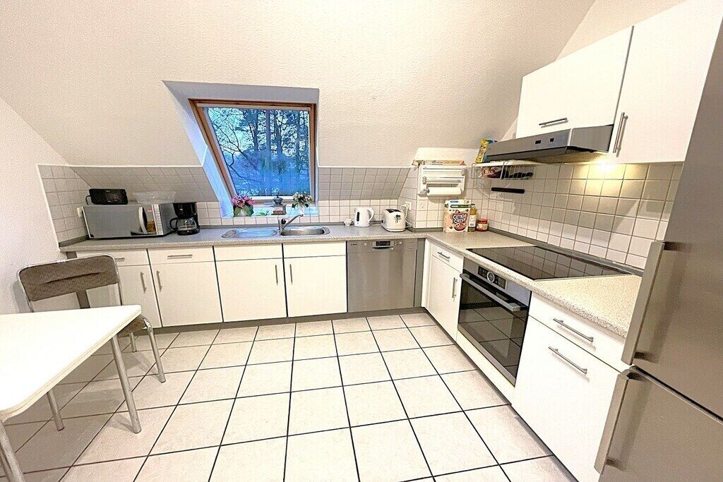 Een kleine keuken met witte kasten, een magnetron, een koffiezetapparaat en een raam met uitzicht op bomen.