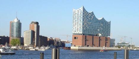 A waterfront cityscape with modern buildings, including a distinctive wavy-roofed structure.