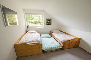 Une petite chambre à coucher composée d’une seule pièce, avec deux lits en bois, une fenêtre et un tableau accroché au mur.