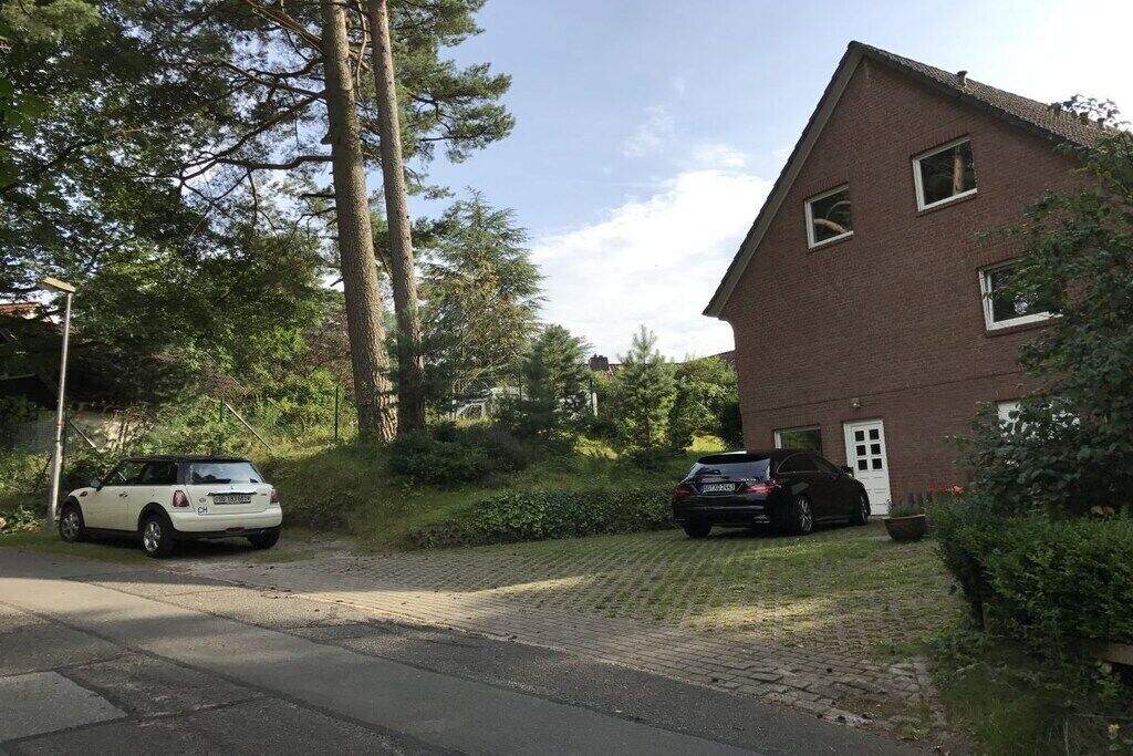 A residential area with two cars parked in front of a brick house with a sloped roof and a small front porch.