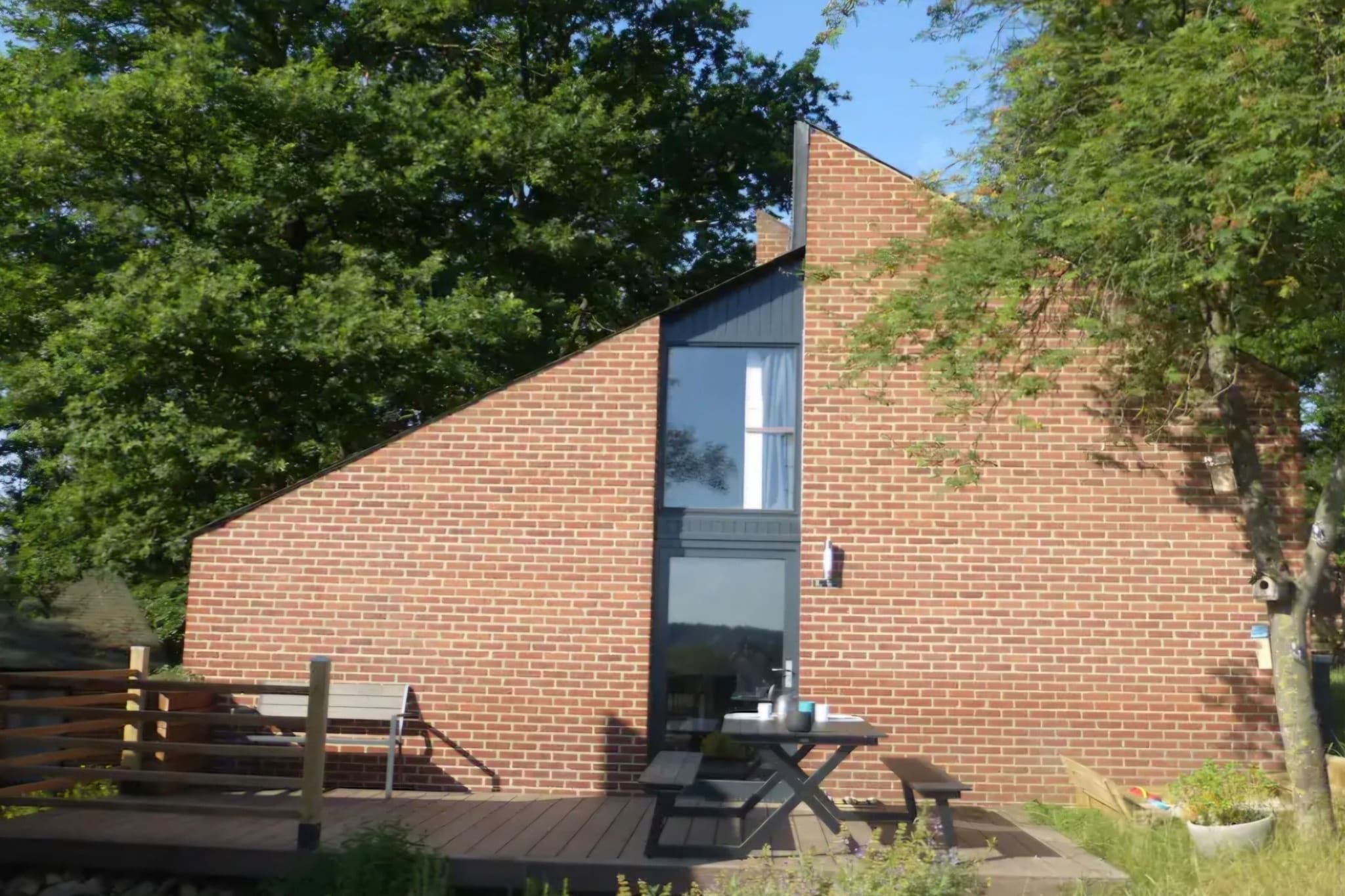 A brick building with a large window, a wooden deck, and a bench.