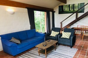 A living room with a blue sofa, two armchairs, a coffee table, and a staircase leading to a dining area. - Charming holiday home with a beautiful view (Blaimont)