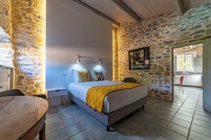 Ein Schlafzimmer mit Bett, Nachttischen, einem Sessel, einem Fenster und einer Steinwand.