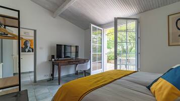 Een slaapkamer met een bed, een bureau met een televisie, een kledingkast en een deur naar een balkon.
