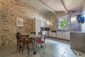 A stone-walled kitchen with a dining table and chairs, a window with a view, and a built-in oven. - Cottage for 2–4 people, Detached, Parking, Pets allowed (NIMES)