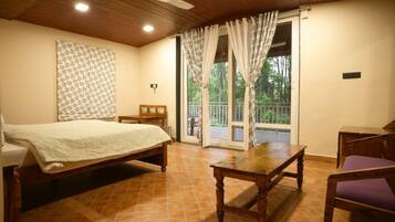 A bedroom with a bed, a wooden table, a chair, and a view of the outdoors through a sliding door.