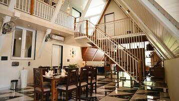 A spacious dining area with a checkered floor, a wooden dining table, and chairs. A staircase with a railing leads to an upper level.