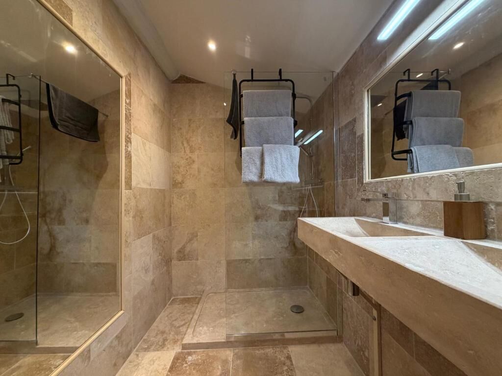 Un baño moderno con cabina de ducha de vidrio, un espejo grande y encimera de mármol.