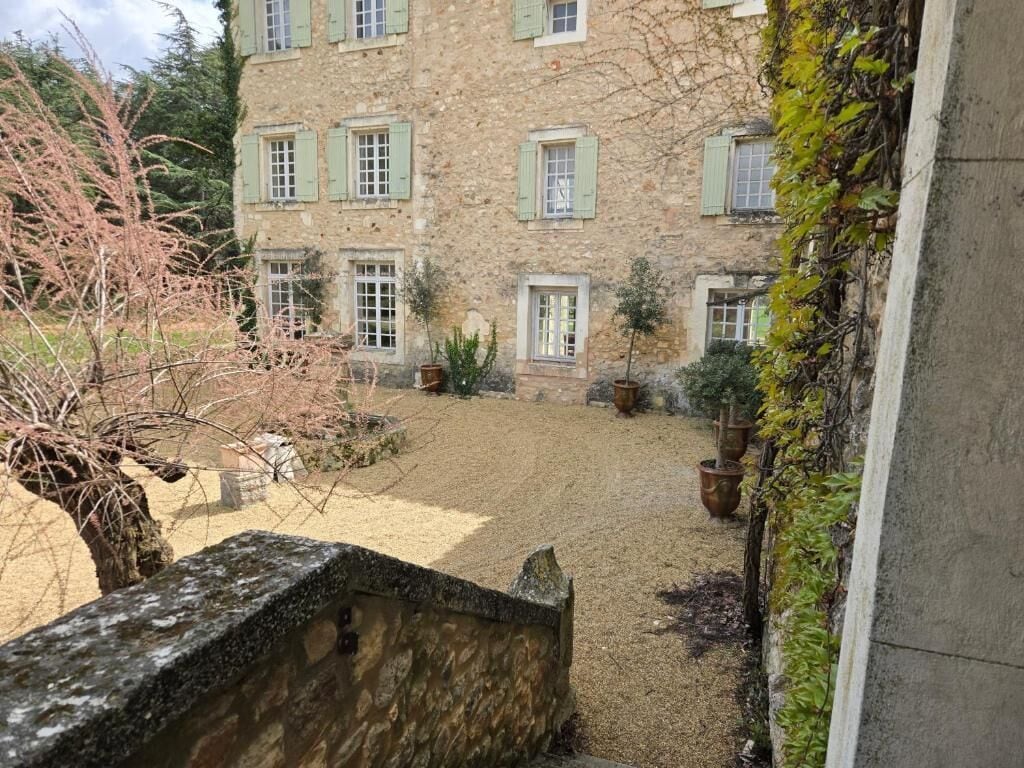 Un bâtiment en pierre doté de nombreuses fenêtres et d’une cour recouverte de gravier.