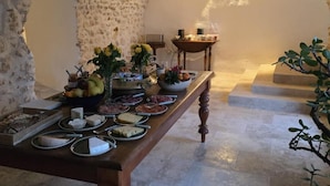 A room with a stone wall, a wooden table with food and drinks, and a small table with a lamp. - Bastide du Luberon (APT)