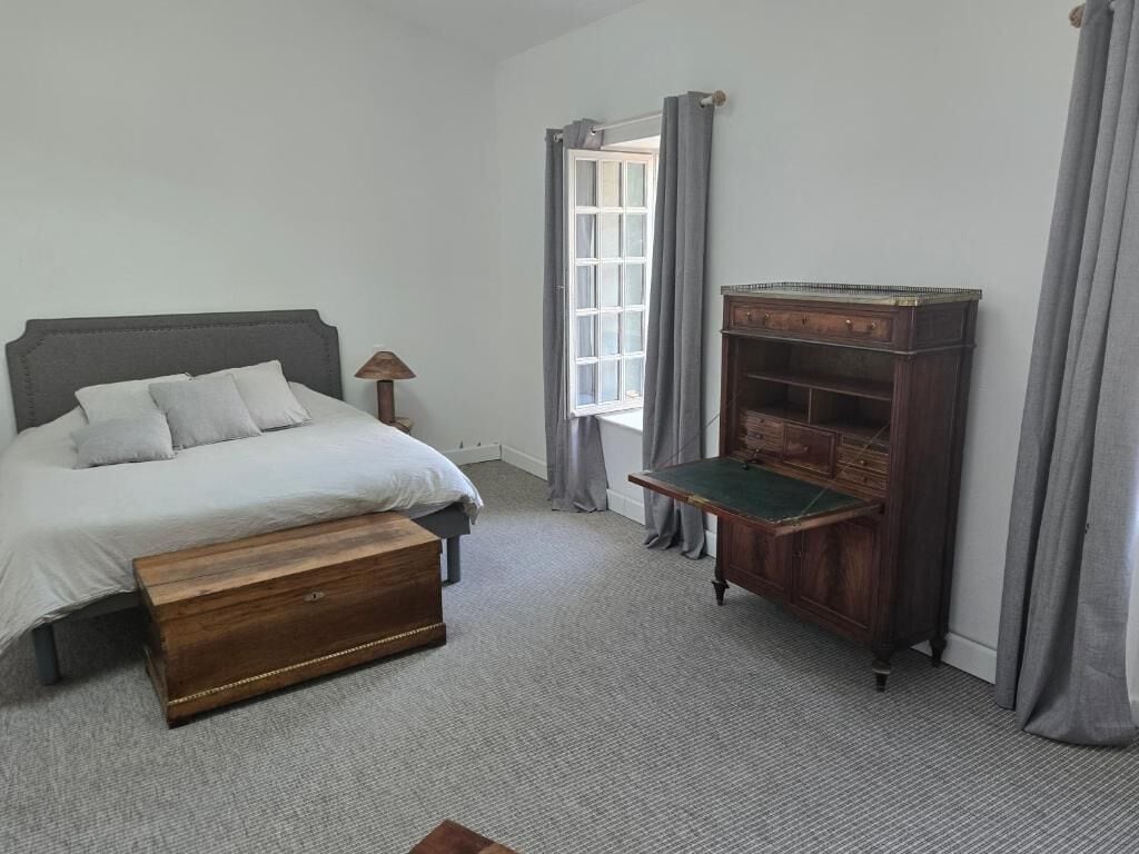 Une chambre à coucher avec un lit, une commode en bois, une table de chevet et une fenêtre avec des rideaux.
