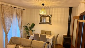 A living room with a sofa, dining table, chairs, a potted plant, a mirror, and a fireplace.