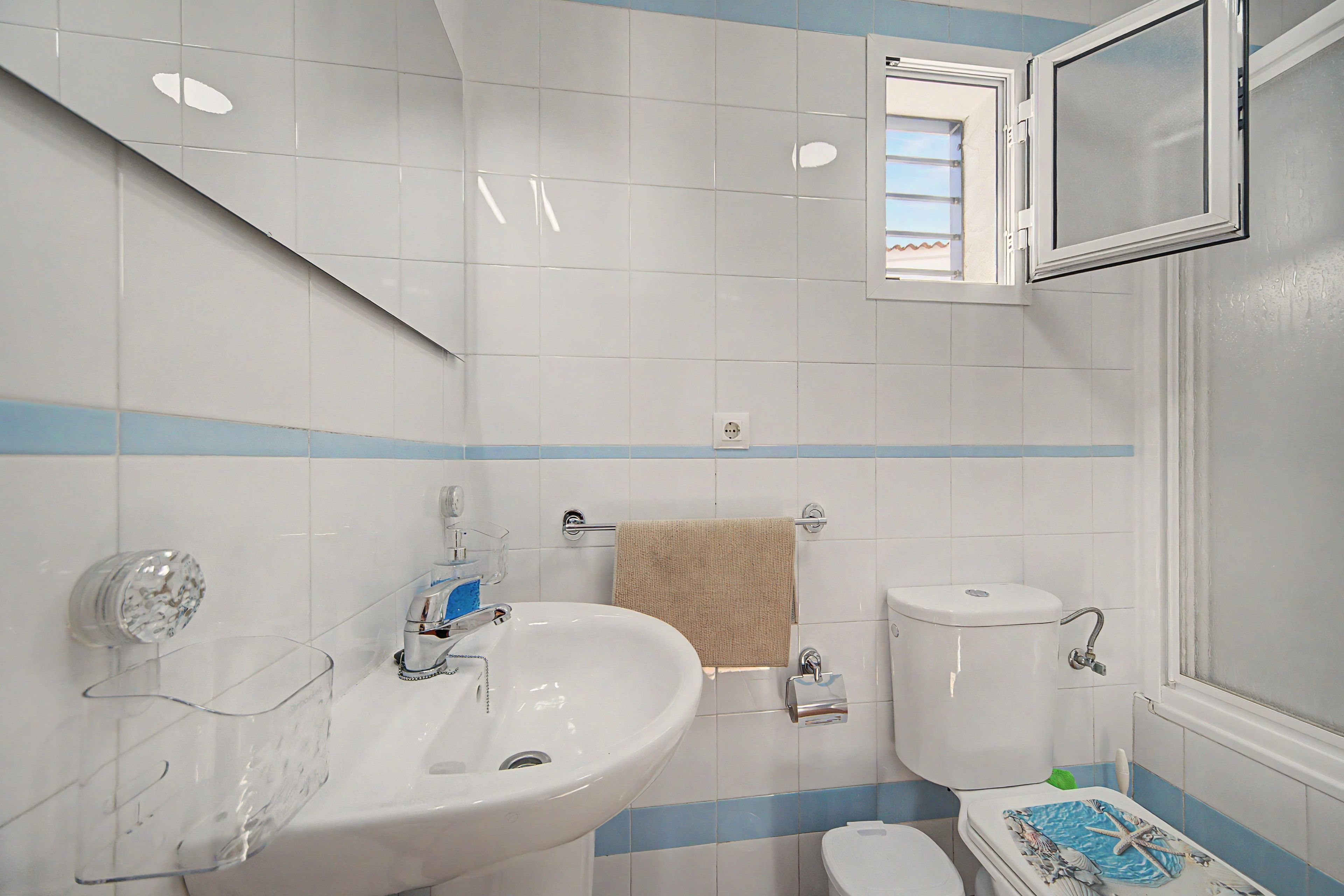 A bathroom with a white sink, a toilet, and a window with a view of the outside.